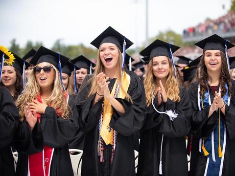 Graduating women in cap and gown clapping